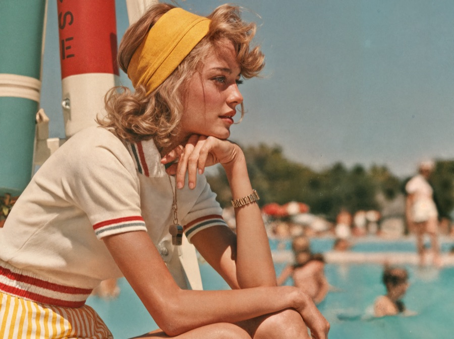 A teenage lifeguard sitting poolside, watching over swimmers