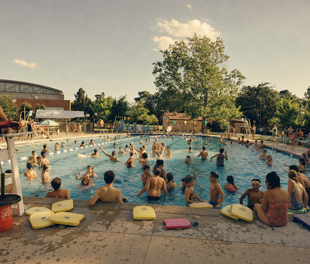 Families and swimmers gathered in the pool at Lowry Swim Club, with kickboards lined up along the pool edge