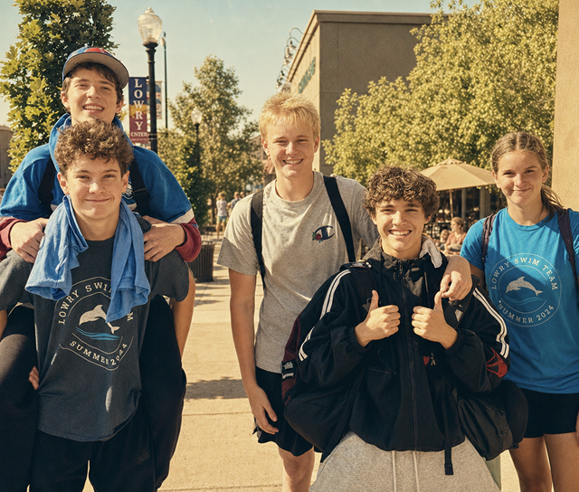A group of Lowry Swim Club teenage staff and teammates smiling together on a sidewalk downtown