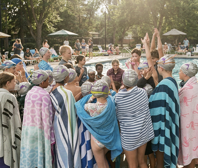 Lowry Swim Team members in caps and towels huddled together poolside before a meet